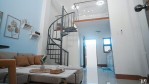 A modern living room with a grey sofa, a coffee table with a plant, and a spiral staircase leading to an upper level. - Woodlands Condotel (Bulan)
