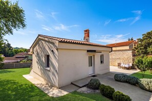 A small, single-story house with a tiled roof, a chimney, and a small front yard with a lawn and a few shrubs. - Susi's Holiday Home, Pula, Croatia (Pula)