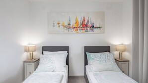 Een hotelkamer met twee bedden, een schilderij van zeilboten en bedlampjes.