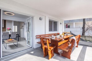 A modern outdoor dining area with a wooden table and benches, a glass door leading to an indoor space, and a view of the surrounding area. - Susi's Holiday Home, Pula, Croatia (Pula)
