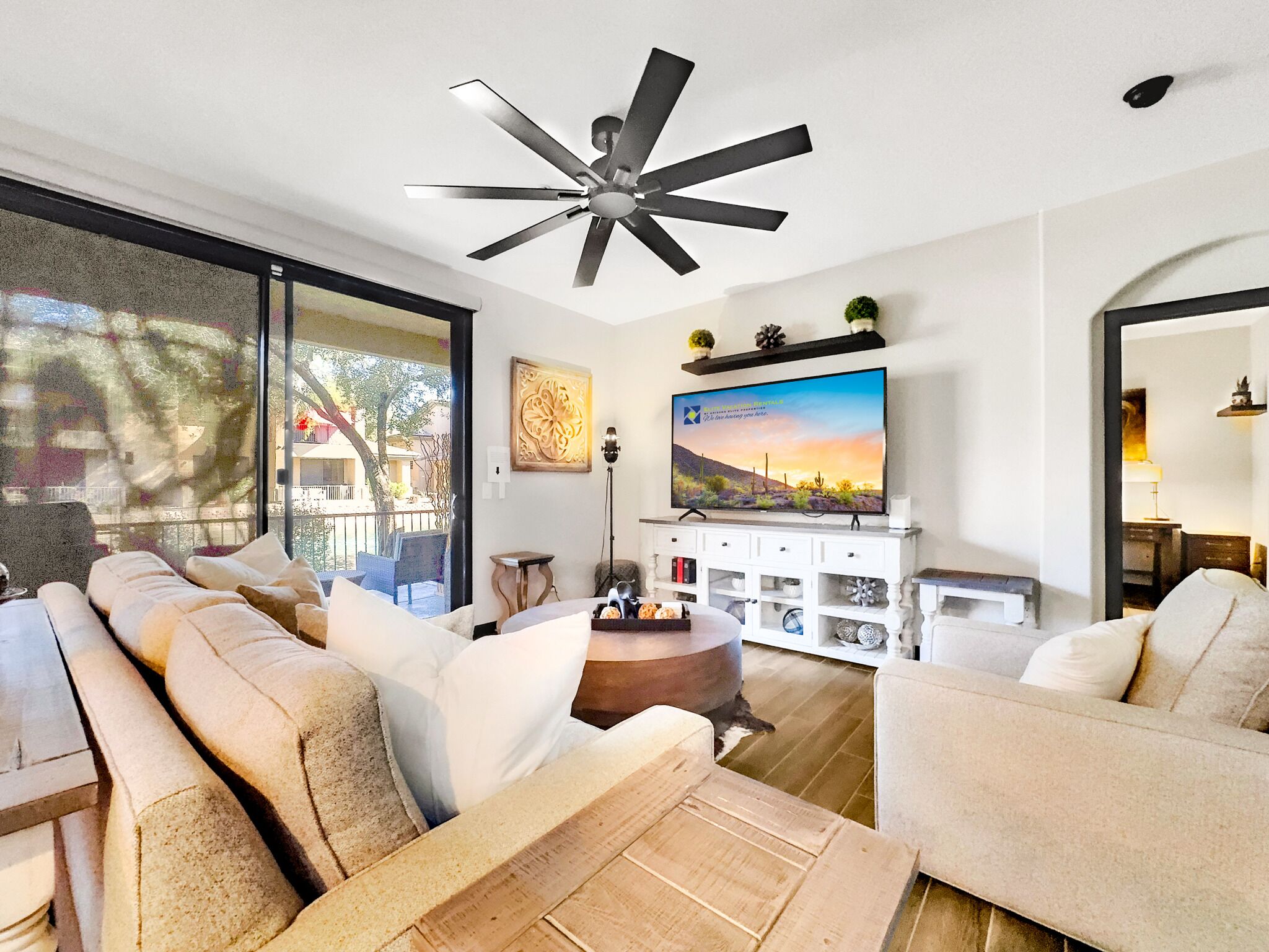 A modern living room with a ceiling fan, a large flat-screen TV, and a sofa set.