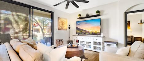 A modern living room with a ceiling fan, a large flat-screen TV, and a sofa set.
