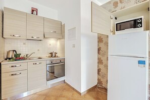 A kitchen with light wood cabinets, a stainless steel sink, a stove, and a white refrigerator.