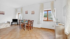 Un vaste espace de vie comprenant une table à manger, des chaises, un canapé, un téléviseur et une fenêtre avec des rideaux.