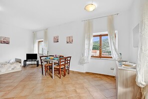 A spacious living area with a dining table, chairs, a sofa, a TV, and a window with curtains.