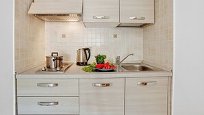 Una cocina moderna con armarios blancos, un lavamanos de acero inoxidable y una encimera con una tetera, una olla y verduras.