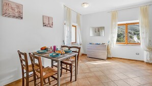 Un coin repas avec une table dressée pour quatre personnes, des chaises, une fenêtre avec des rideaux, un miroir et une commode.