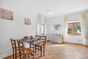 A dining area with a table set for four, chairs, a window with curtains, and a view of a mountainous landscape.