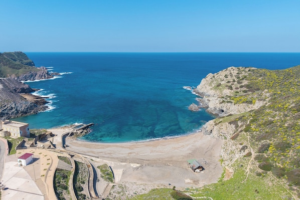 A coastal landscape with a clear view of the sea, rocky terrain, and a paved area with buildings.