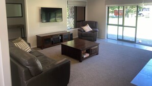 Un salon comprenant un canapé, un fauteuil, une table basse, un téléviseur et une porte-fenêtre coulissante.