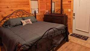 Ein Schlafzimmer in einer Holzhütte mit einem Bett, einem Schminktisch, einem Spiegel und einer Tür mit Fenster.