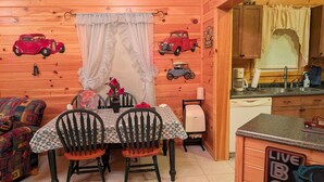 Ein gemütliches Holzhaus-Interieur mit Esstisch, Stühlen, einer kleinen Küchenzeile und dekorativen Automodellen an den Wänden.