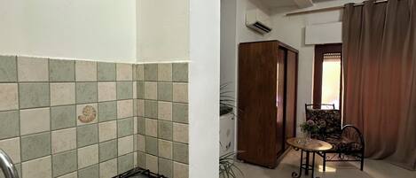 A kitchen with a granite countertop, stainless steel sink, and a tiled backsplash. There is a framed picture on the wall and a dining area with a table and chairs.