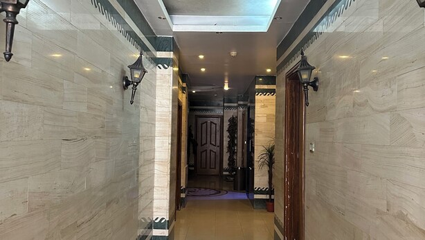 A hallway with patterned floor tiles, wall-mounted lights, and a ceiling with recessed lighting. - Al Majd Hotel  (Amman)