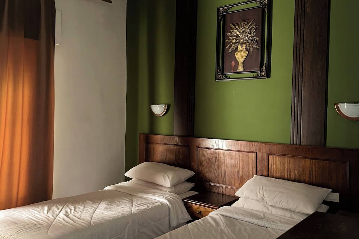A hotel room with two beds, a wooden headboard, a green accent wall, and a framed artwork above the beds.