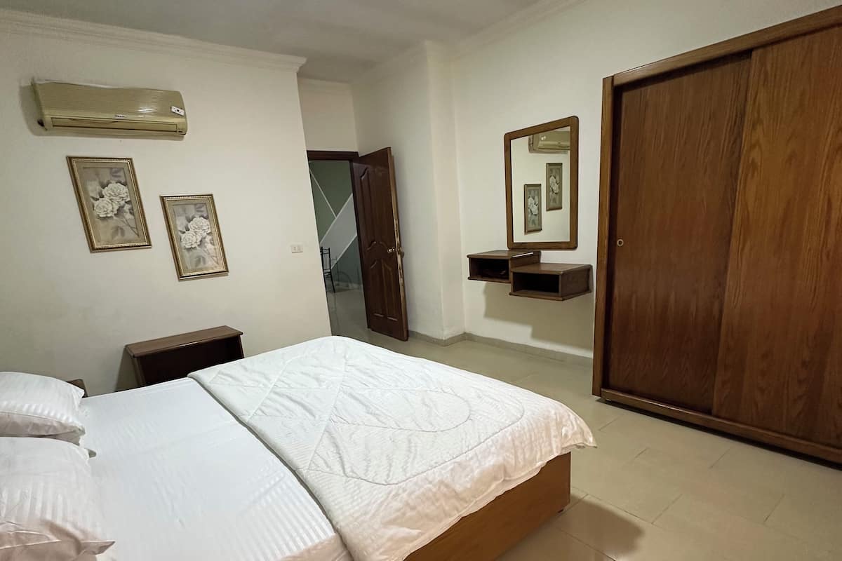 A bedroom with a bed, a wooden wardrobe, a mirror, and two framed pictures on the wall.