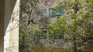 A balcony with a table and chair, overlooking a building with multiple windows and trees. - Al Majd Hotel  (Amman)