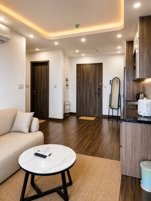 A modern living room with a sofa, a round coffee table, and a kitchen area with wooden cabinets and a countertop. - X-Stay Bloom (Hai Phong)