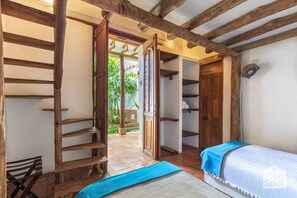 Ein Zimmer mit einem Bett, einem Holzstuhl, einem Kleiderschrank und einer Tür zu einem Außenbereich.