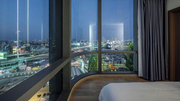 A modern hotel room with a curved bed, large windows offering a city view, and a view of the cityscape at night. - LANDMARK 81 Signature Residence (Ho Chi Minh City)