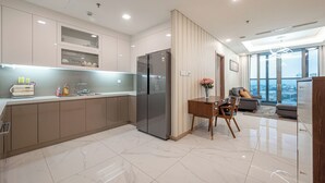 A modern kitchen with a built-in refrigerator, a dining area with a wooden table and chairs, and a view of the city through large windows. - LANDMARK 81 Signature Residence (Ho Chi Minh City)