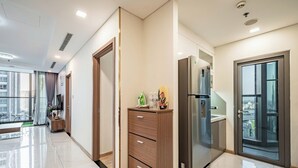 A modern hotel room with a large window, a minibar, and a sliding glass door to a balcony. - LANDMARK 81 Signature Residence (Ho Chi Minh City)