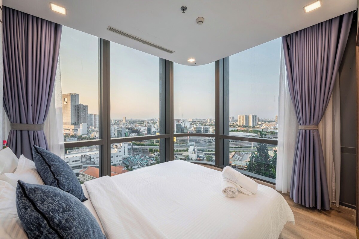 Une chambre d’hôtel dotée d’un grand lit, offrant une vue sur le paysage urbain grâce à de larges fenêtres du sol au plafond, et présentant un design moderne au niveau du plafond.