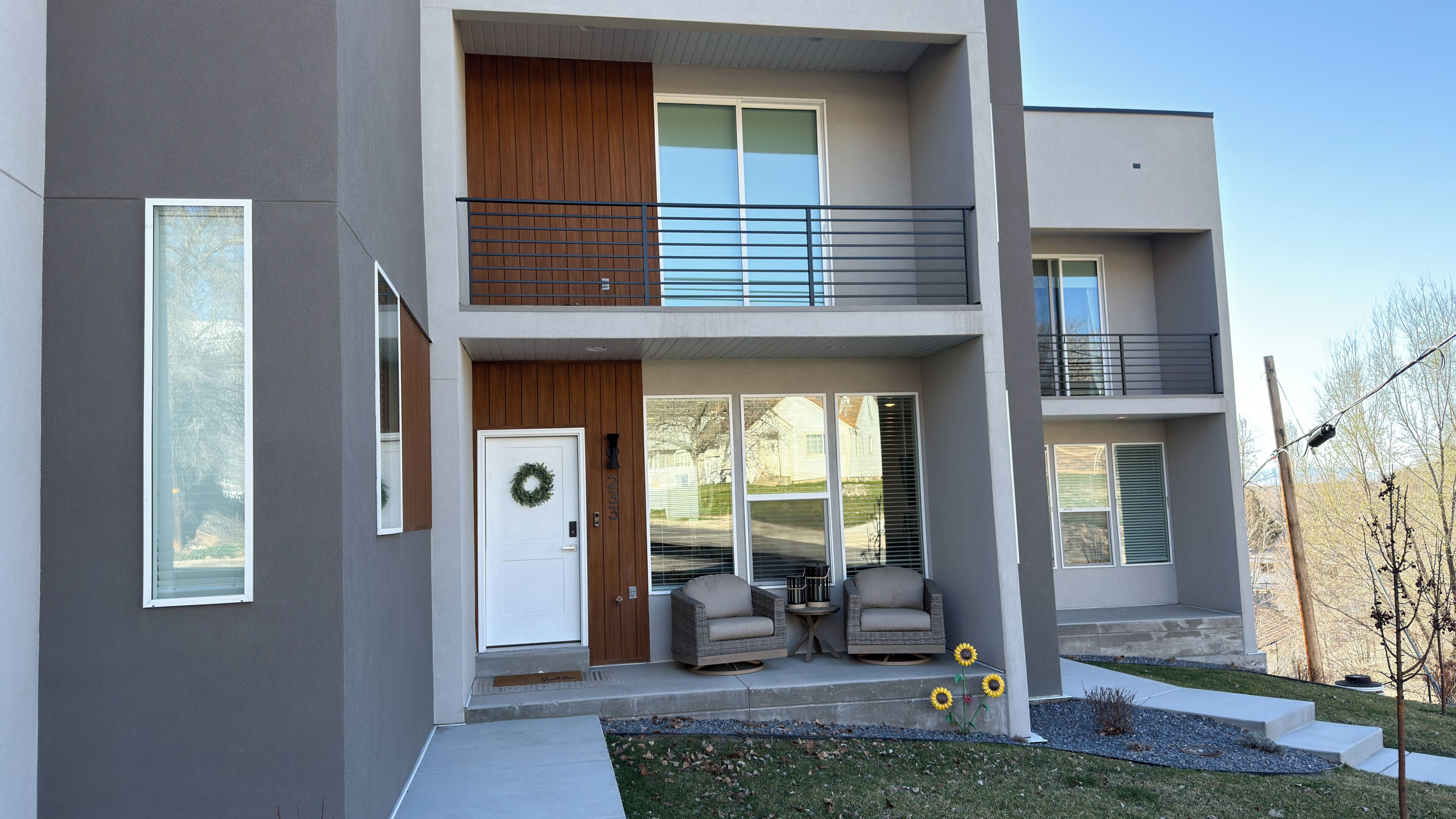 A modern two-story building with a balcony, a door with a wreath, and outdoor seating.