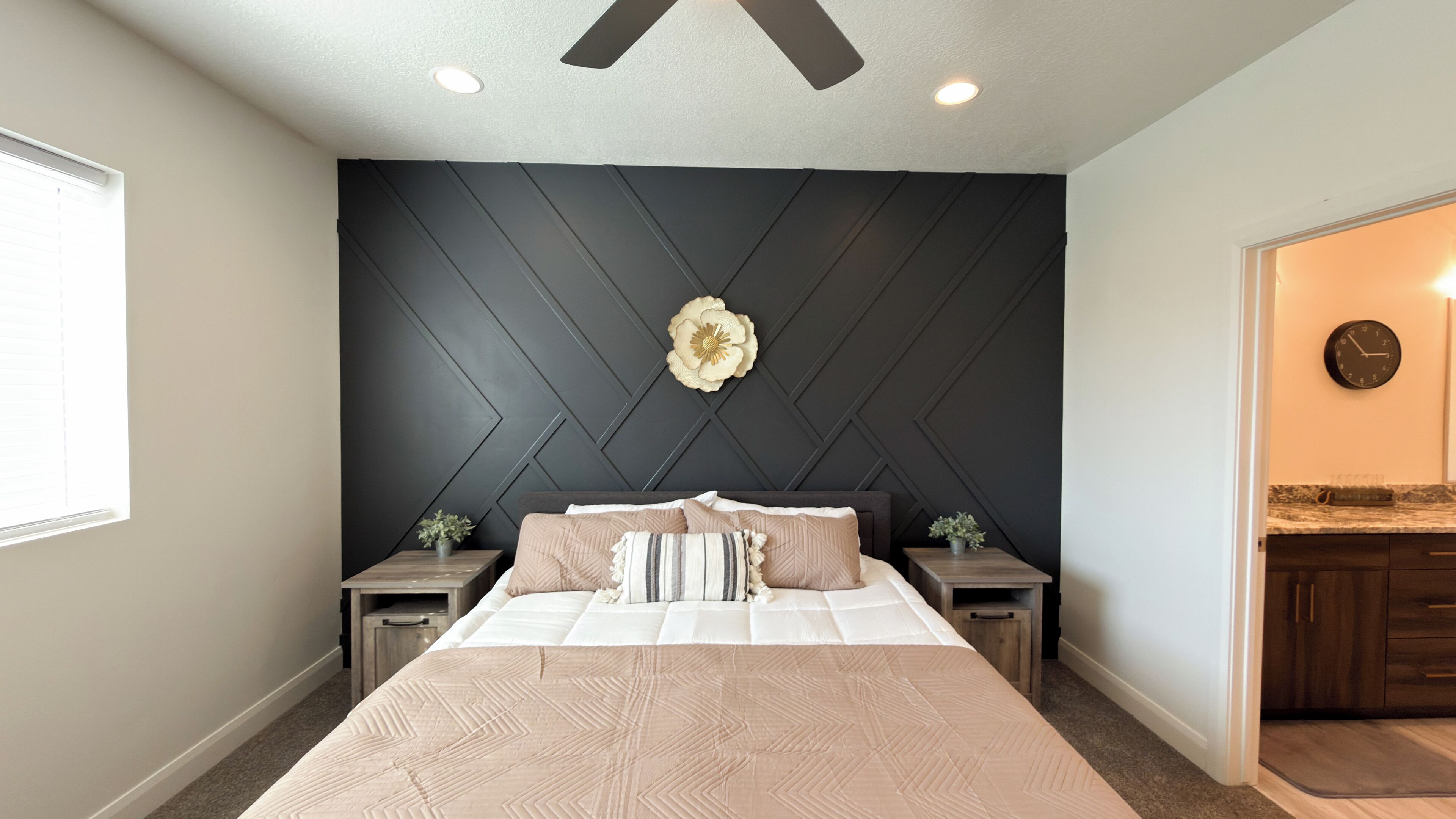 A bedroom with a bed, nightstands, a decorative wall panel, a flower, and a clock.