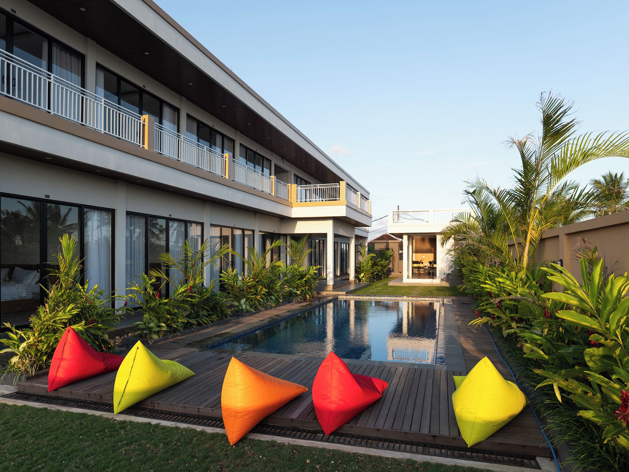 Un hotel moderno con piscina, zona de estar exterior y abundante vegetación.