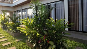 A modern building with large windows, a balcony, and a well-maintained garden with various plants. - Pondok Uma Jero (Tabanan)