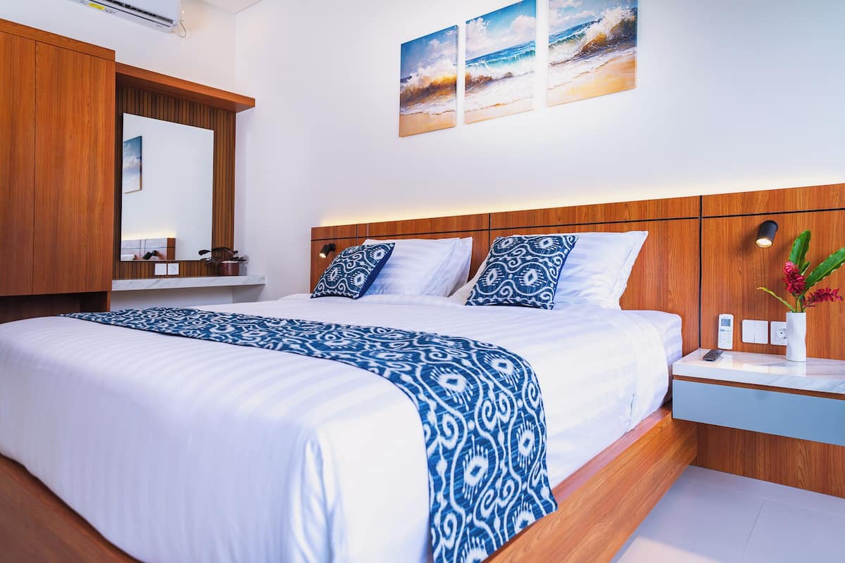 A hotel room with a large bed, wooden headboard, a bedside table with a vase, and a wall-mounted mirror.