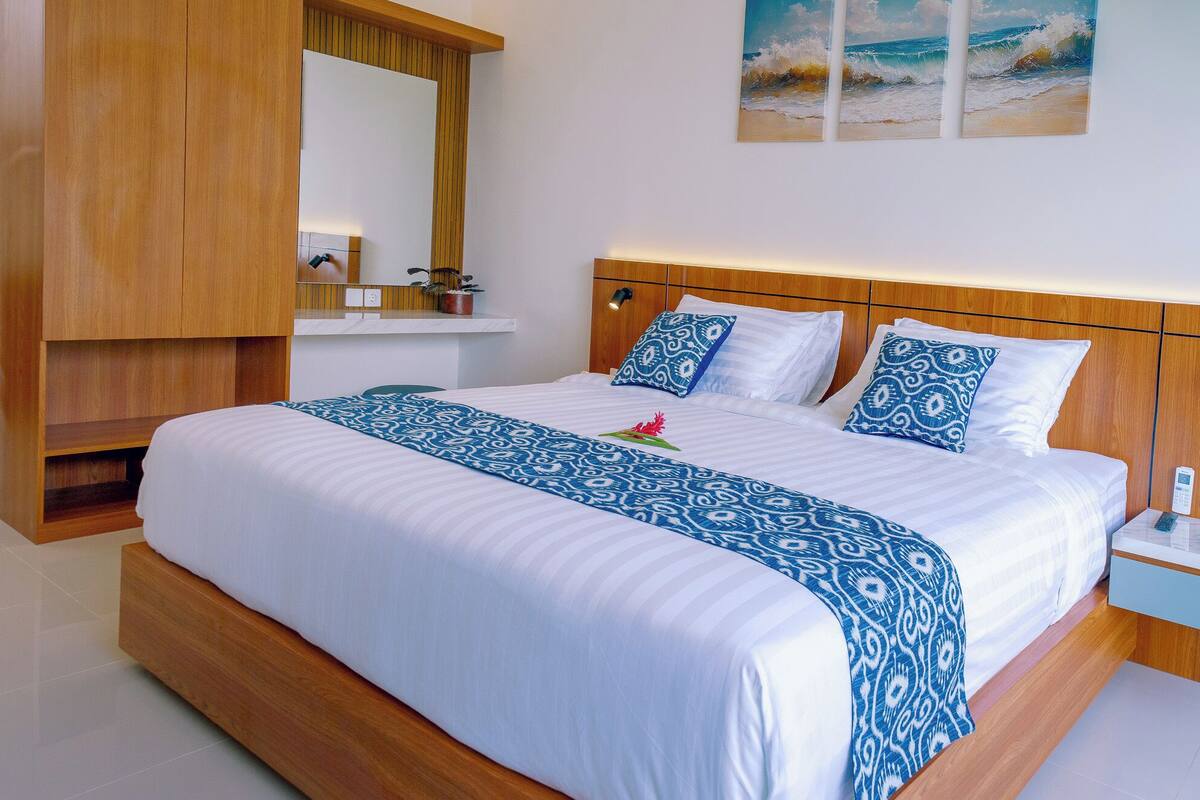 A hotel room with a large bed, wooden headboard, a mirror, a bedside table, and a wall-mounted painting.