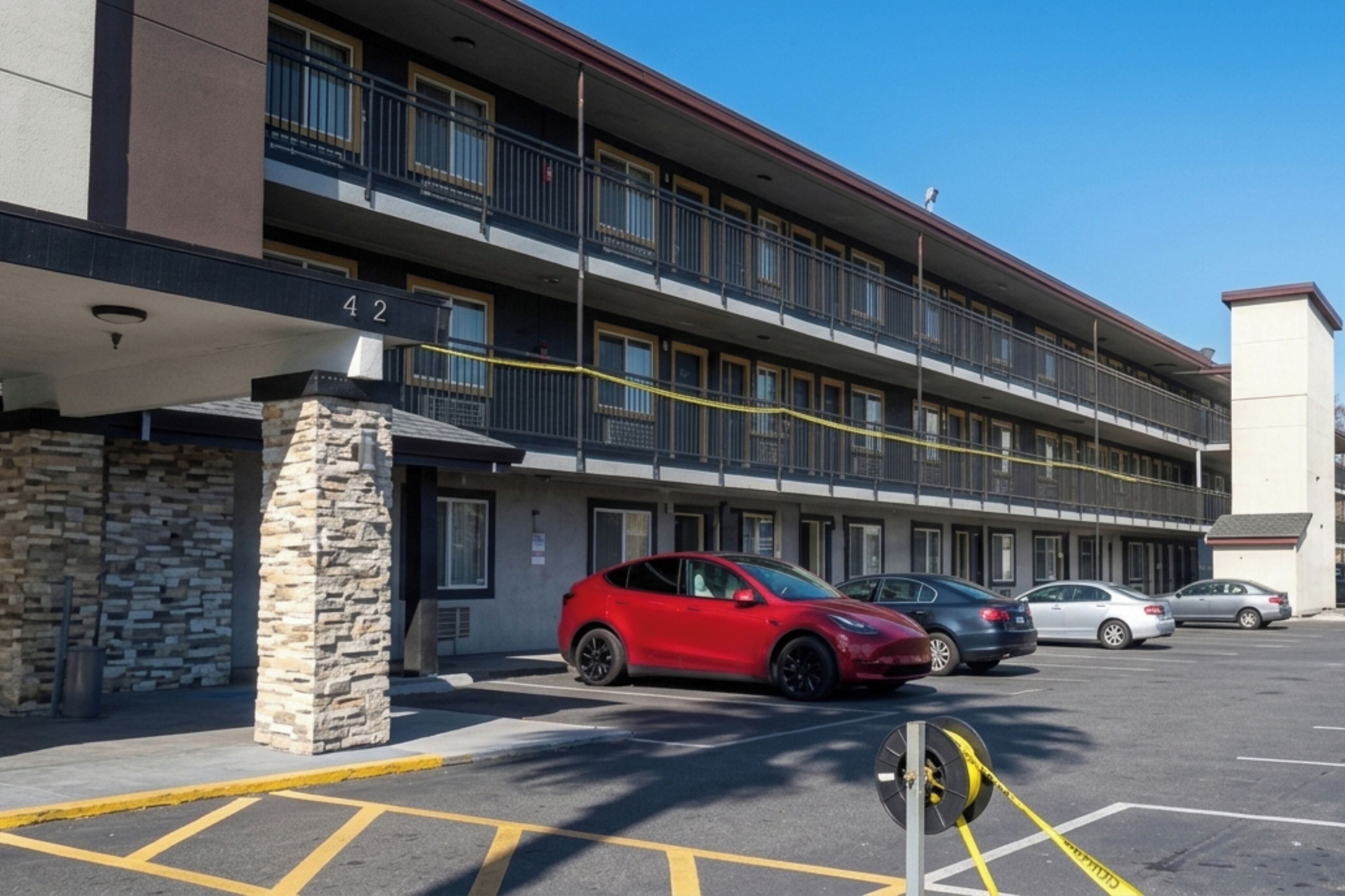 A multi-story building with a stone pillar, a red car, and several parked cars.