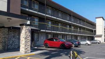 A multi-story building with a stone pillar, a red car, and several parked cars.