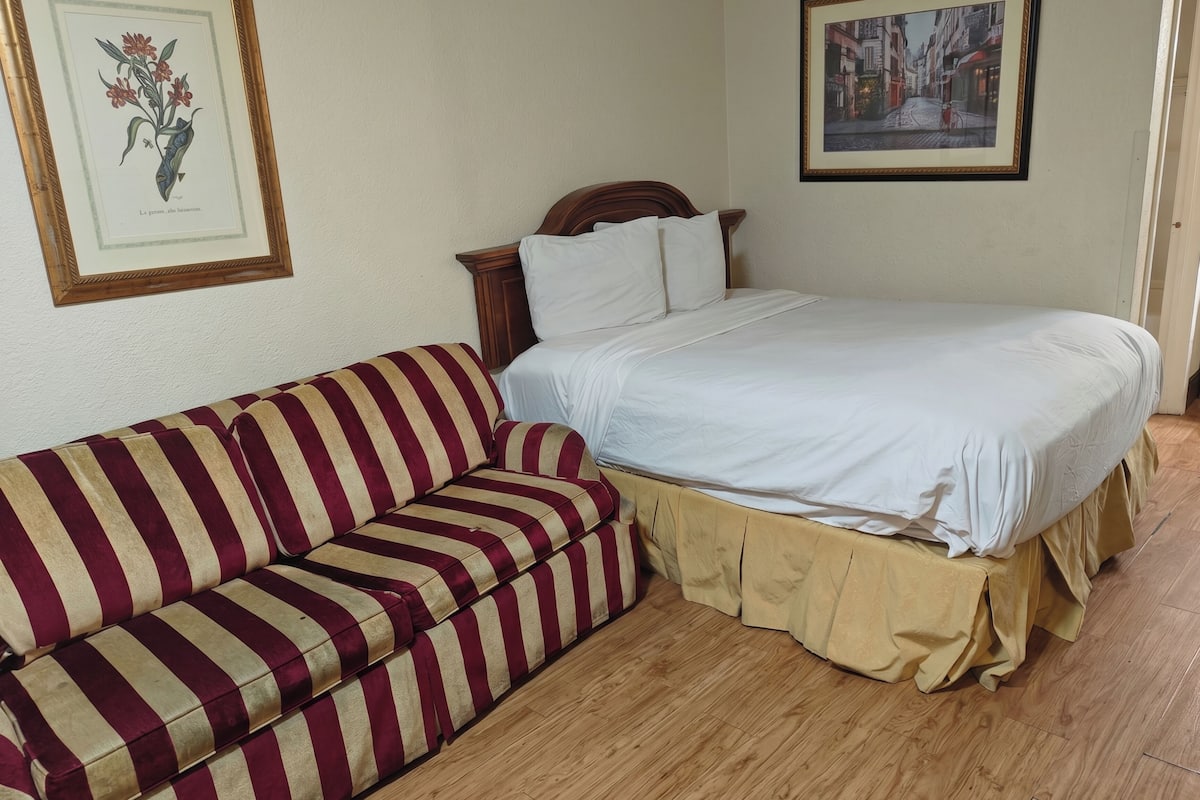 A room with a bed, a striped sofa, and two framed pictures on the wall.