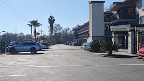 Um estacionamento com vários carros, um edifício com sacadas e palmeiras ao fundo.
