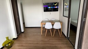 A modern living room with a wooden coffee table, two white chairs, a TV mounted on the wall, and a wooden floor.