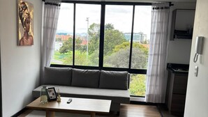 A modern living room with a large window, a sofa, a coffee table, and a yellow vase.