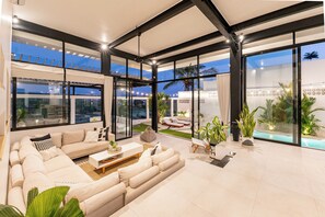 A modern living room with a large sofa, a coffee table, and a view of a pool and outdoor seating area. - Villa Bali Escape– Private Ricefield Retreat, Steps from the Canggu Action (Canggu)