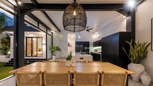 A modern dining area with a wooden table and wicker chairs, a hanging light fixture, and potted plants. - Villa Bali Escape– Private Ricefield Retreat, Steps from the Canggu Action (Canggu)