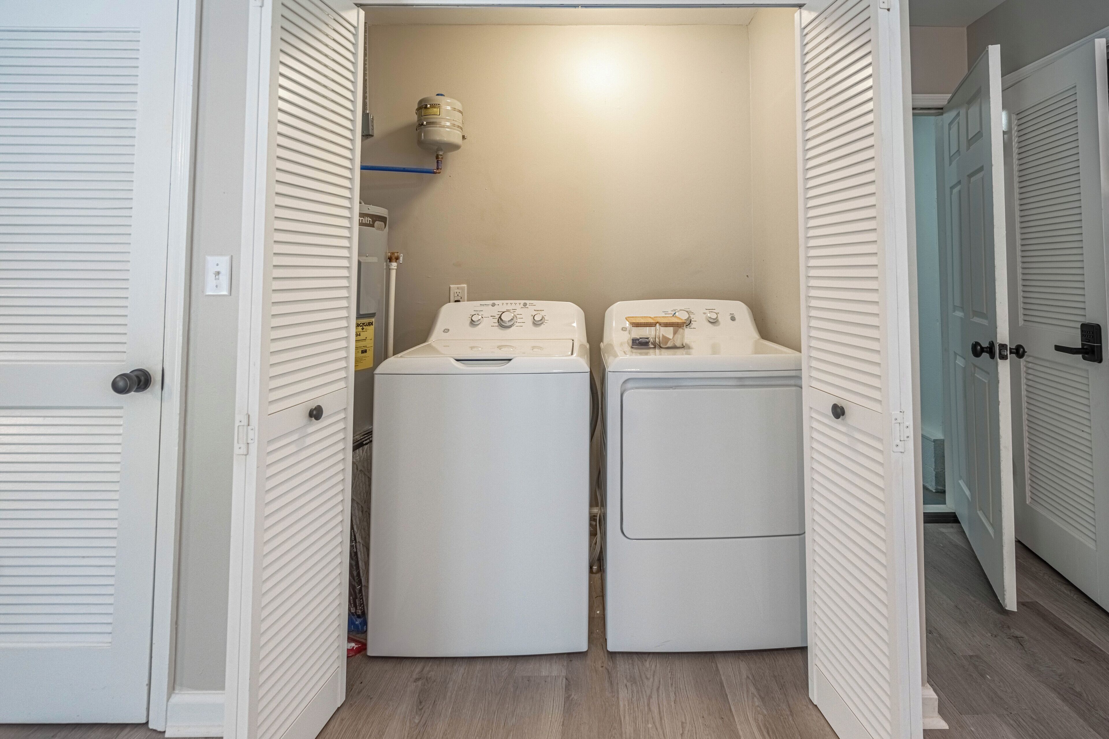 A laundry room with two white front-loading washers and dryers, a water heater on the wall, and a blue shelf above the dryers.