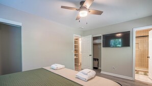 A bedroom with a bed, a ceiling fan, a TV, and a walk-in closet.