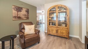 A brown leather armchair with a decorative pillow, a wooden cabinet with glass doors, and a painting on the wall.
