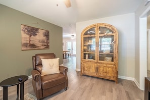 Un fauteuil en cuir marron agrémenté d’un coussin décoratif, un meuble en bois aux portes vitrées et un tableau accroché au mur.