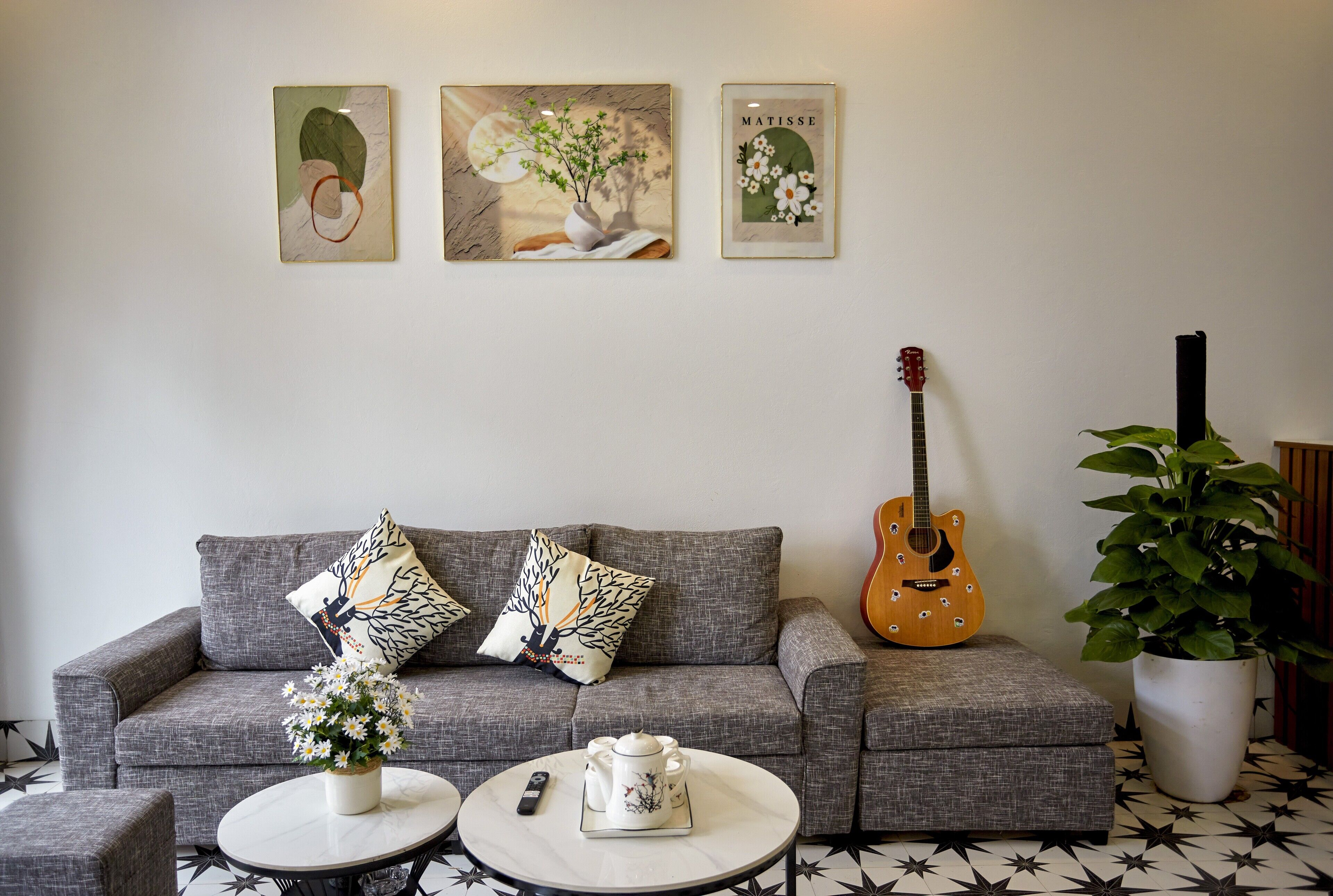 Una sala de estar con un sofá gris, dos mesas redondas, una guitarra y una planta en maceta.