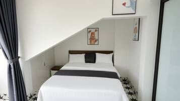 A bedroom with a bed, a nightstand, a window with curtains, and a wall with framed artwork.