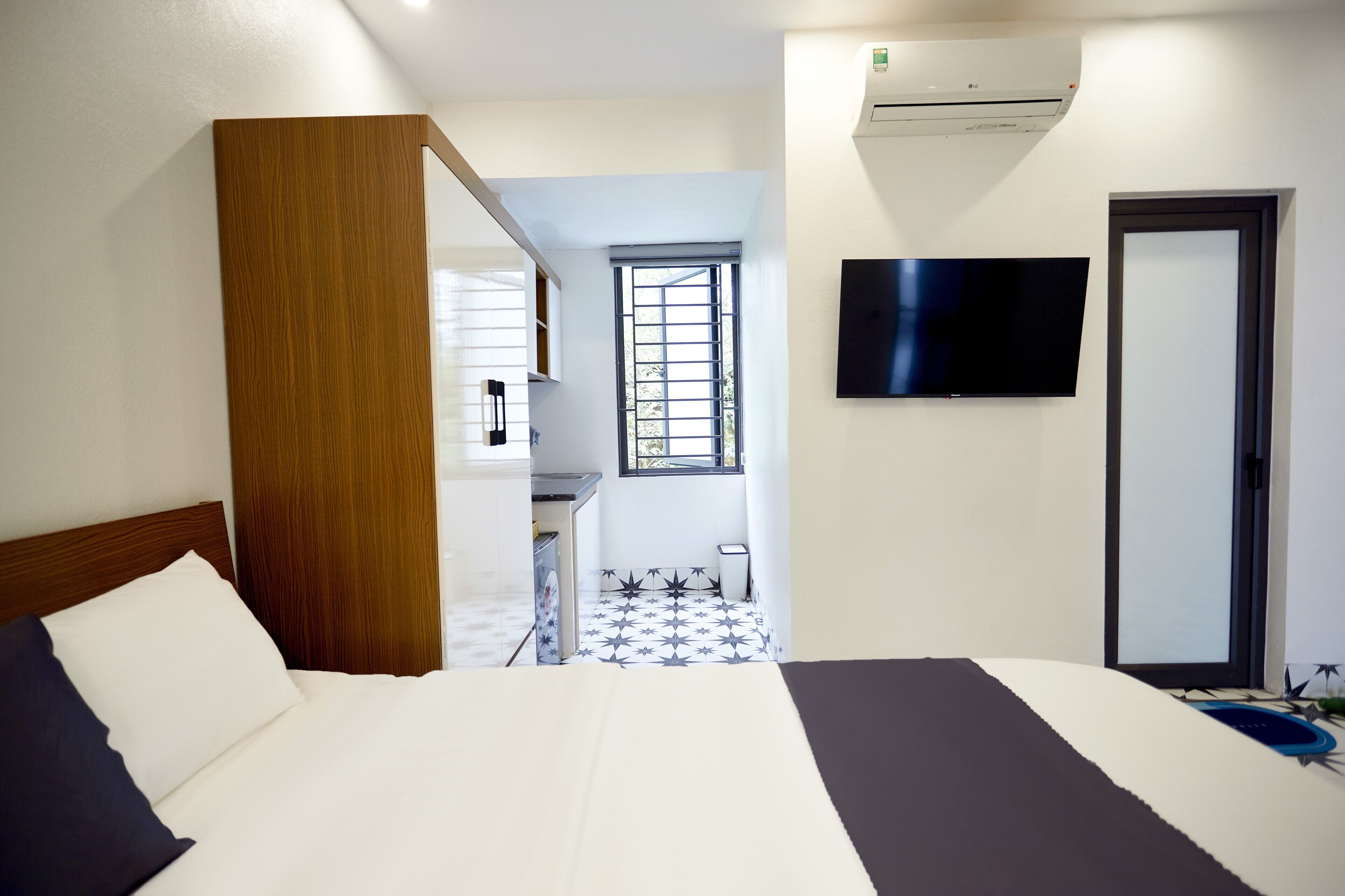 A hotel room with a bed, a TV mounted on the wall, and a window with blinds.