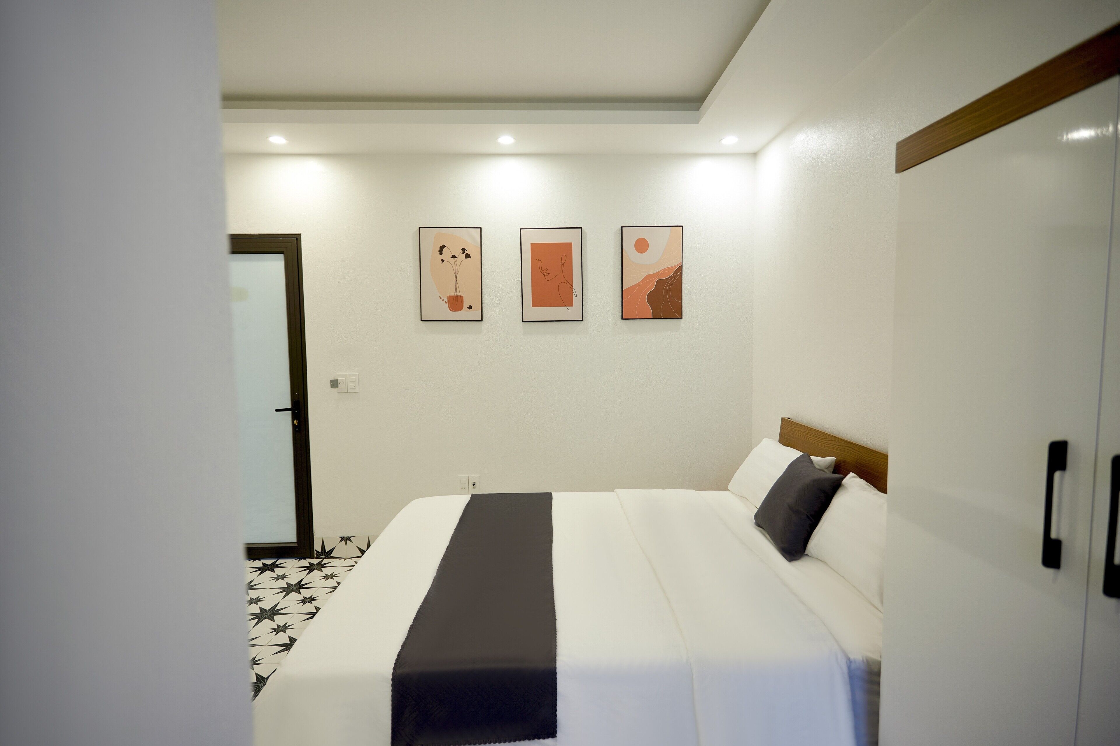 Habitació d'hotel amb un llit, una taula de nit negra, un armari i tres quadres a la paret.