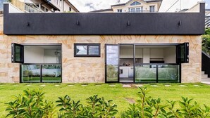 Una casa moderna de dues plantes amb grans portes i finestres de vidre, façana de pedra i jardí ben cuidat.